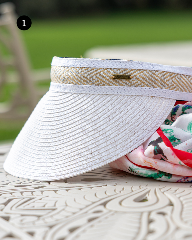 Women's straw sun visor with woven detail in white sitting on a scarf and outdoor table. 