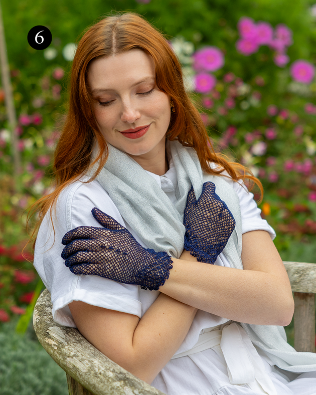 Woman wearing cotton crochet gloves in navy with silver scarf in the garden. 