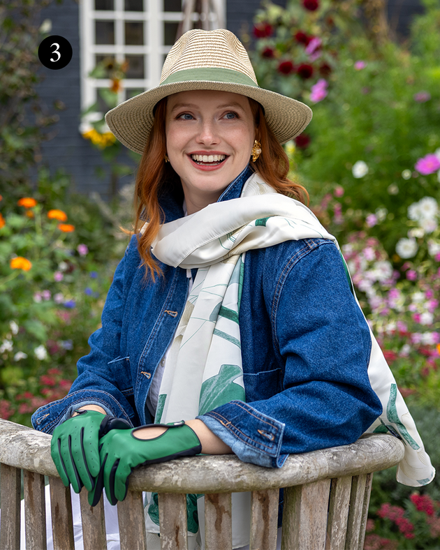 Woman wearing green and ivory scarf with straw hat and leather gloves. 