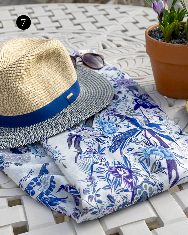 Women's Chinoiserie Flowers and Birds Lightweight Scarf with Borders sitting on a table with a straw hat. 