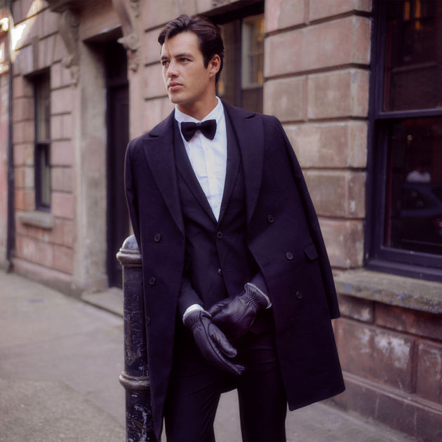 man wearing deer skin gloves, a tuxedo and long wool coat 